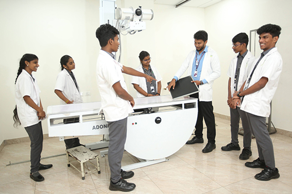 Medical students in white coats surround a large radiology machine as one person points to it.